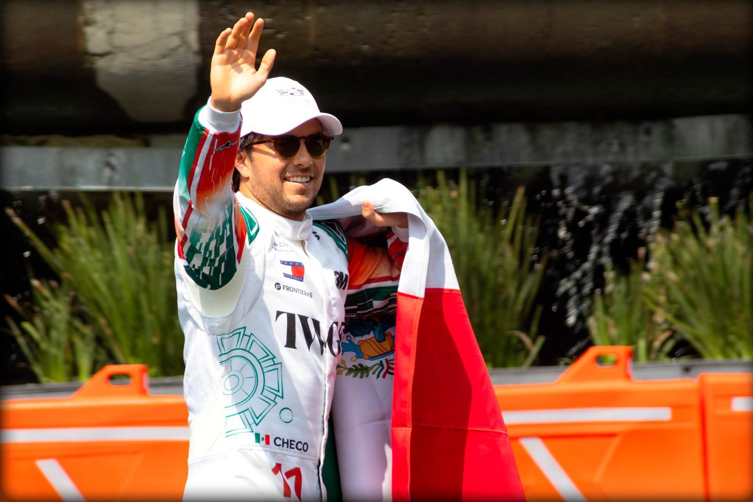 Checo Pérez saluda a los aficionados sosteniendo la bandera de México